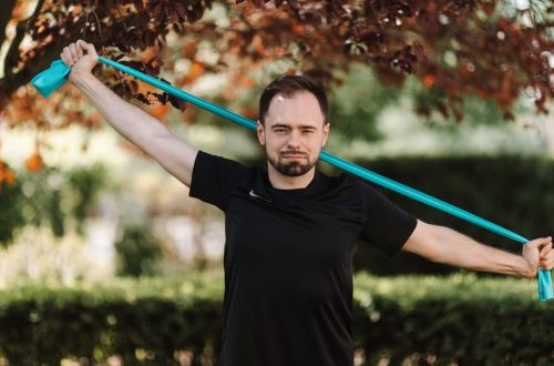 Adult man in black shirt exercises with a resistance band outside.
