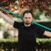 Adult man in black shirt exercises with a resistance band outside.