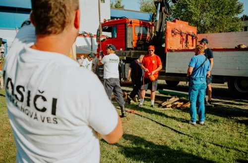 A group of firefighters in a park setting during a public demonstration near a fire truck.